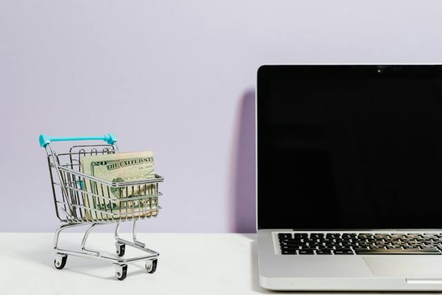small shopping cart with money next to computer